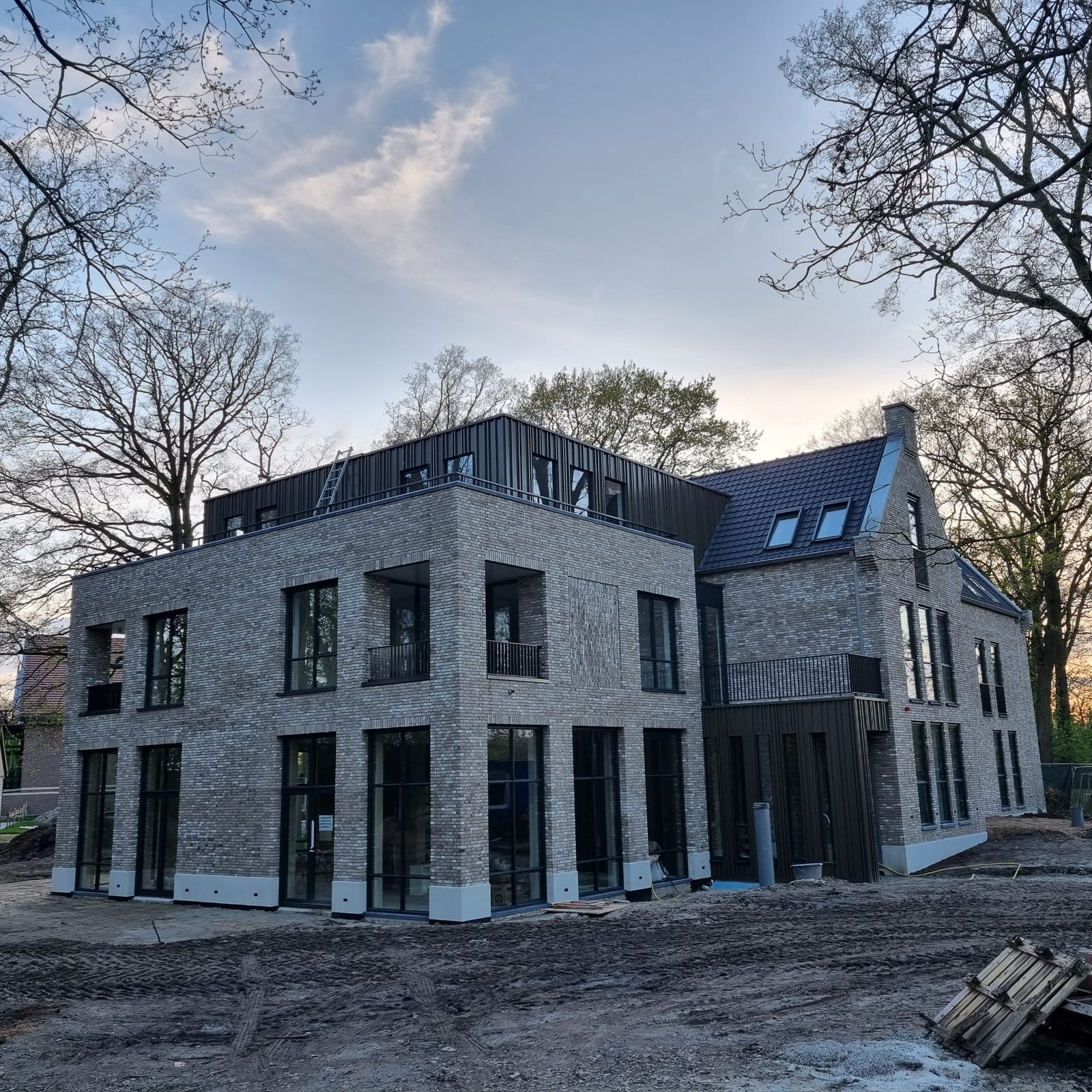 Nieuwbouw van Aannemersbedrijf A. Fekken B.V. bij schemer, met metselwerk, zwart zinkwerk en grote raampartijen